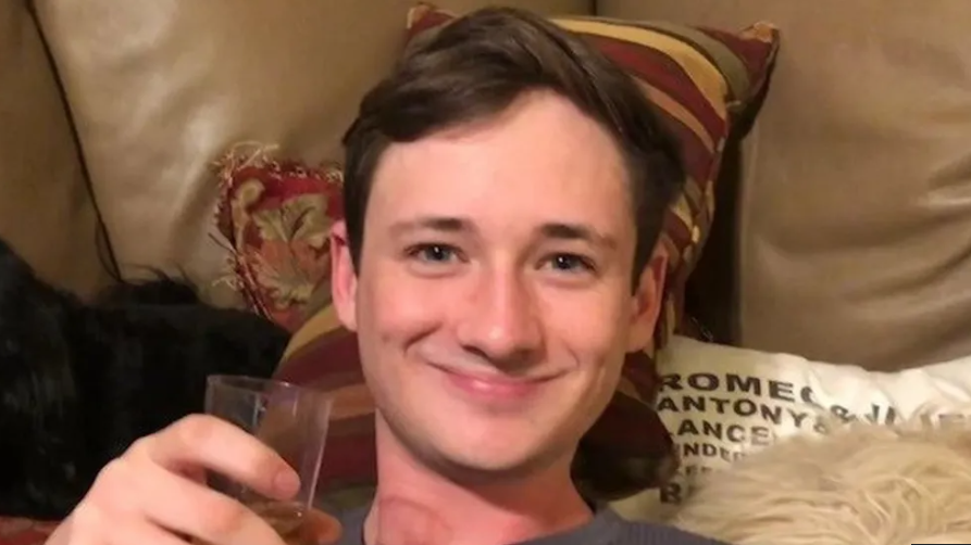 Blaze Bernstein smiles at the camera while holding a glass in his hand.