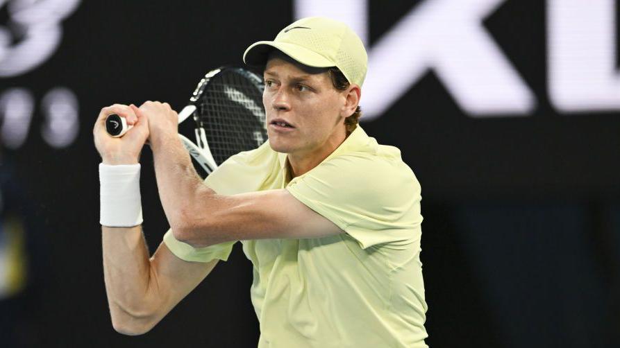 Jannik Sinner holds a tennis racquet over his shoulder