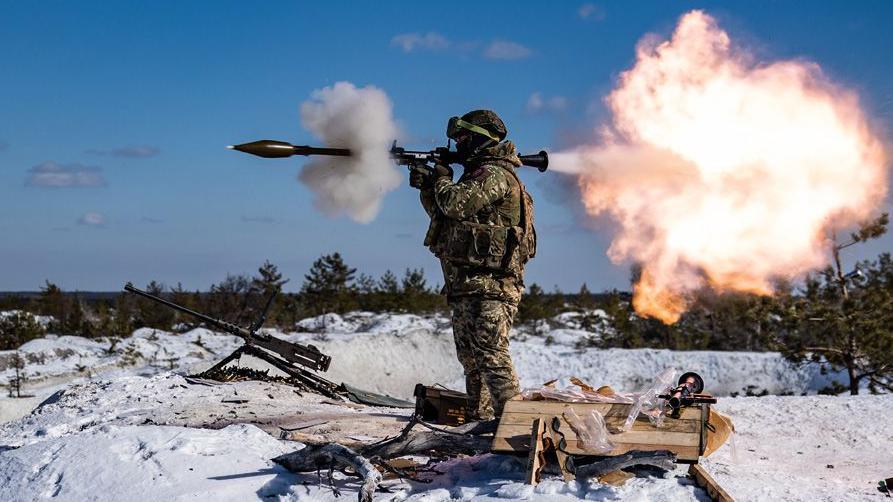 A soldier facing left and fires a weapon in the same direction, releasing a ball of fire behind it. The ground is icy and there is a gun next to the soldier. The sky is blue.