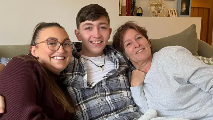 Jayme Guthrie, Ted Spurrell and Sasha Spurrell pictured on a sofa together after Ted's accident. Jayme, on the left, is wearing a glasses and a maroon jumper. Ted, in the middle, has brown hair and is wearing a checked shirt and white t-shirt. Sasha, on the right, has short brown hair and is wearing a grey jumper.