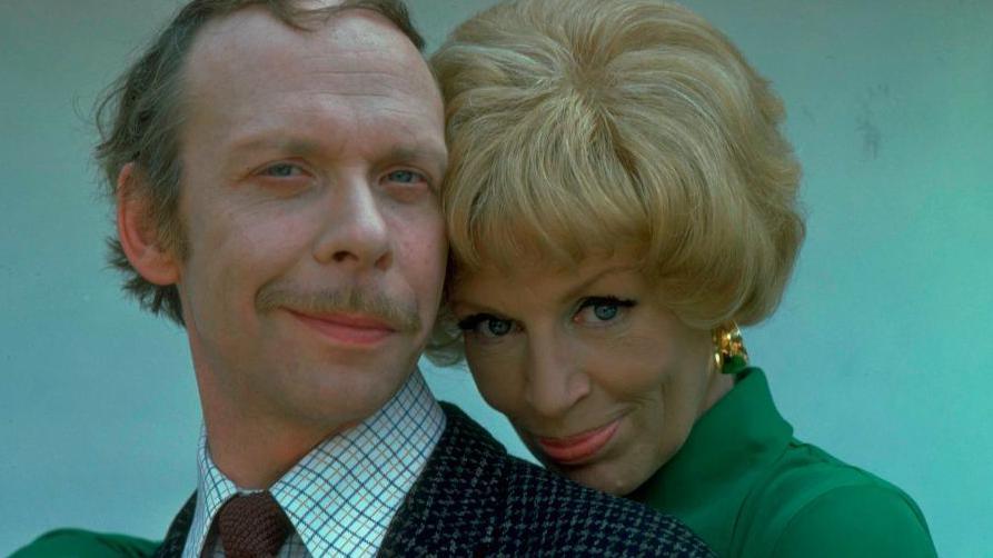 Brian Murphy in a suit being embraced by Yootha Joyce