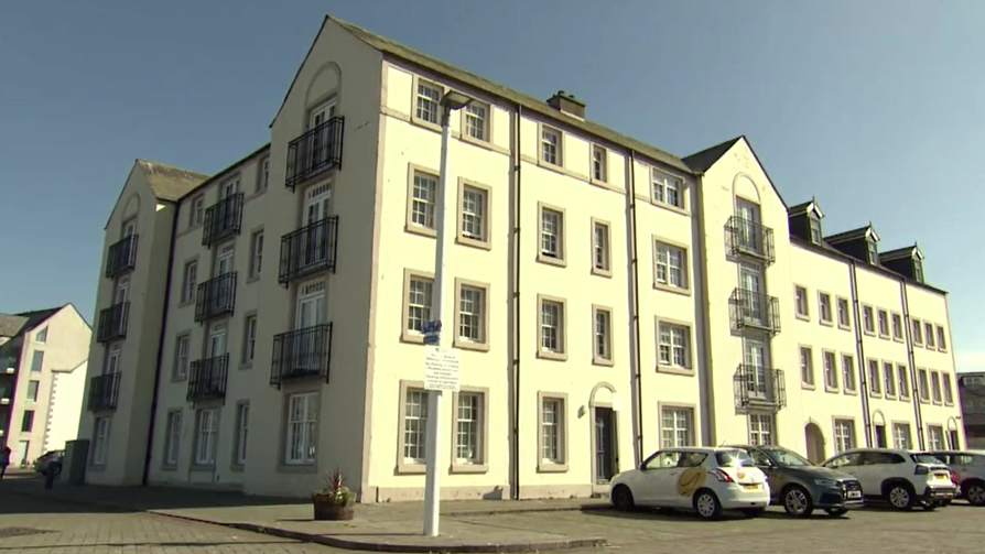 A four-storey white apartment building with cars parked alongside it.