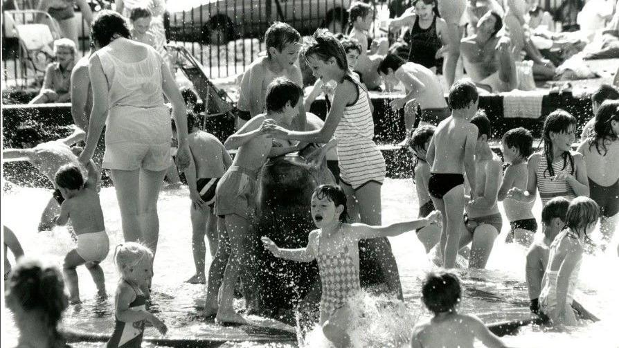 A black and white image of large numbers children and adults using the pool