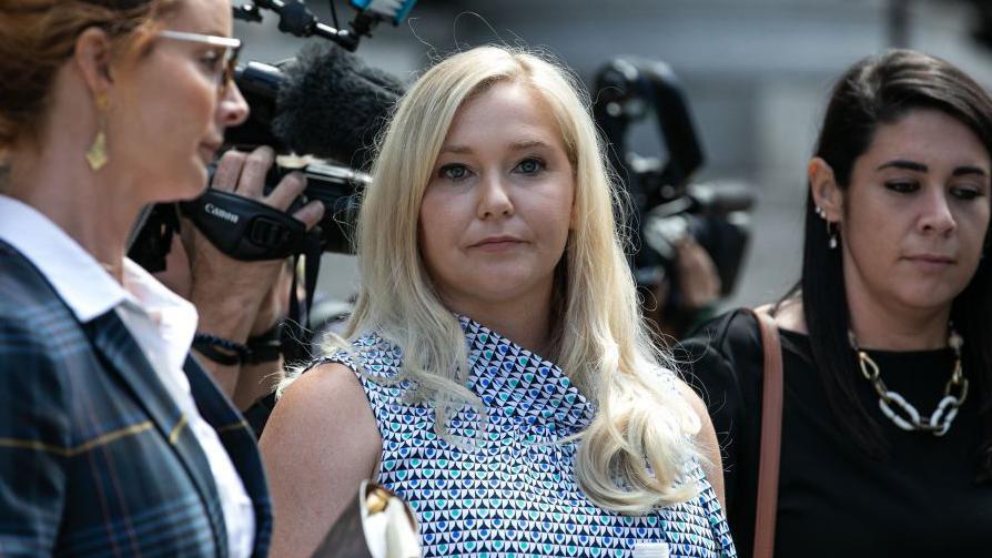 Virginia Giuffre pictured outside court in 2019. She is in the centre of the image and looking directly at the camera. Television cameras appear behind her.