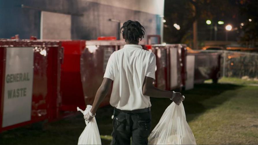 A man carries two bags of rubbish to rubbish bins