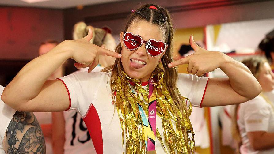 Jess Breach, wearing heart-shaped sunglasses with her name written on and her World Cup winner's medal around her neck, along with gold ribbons
