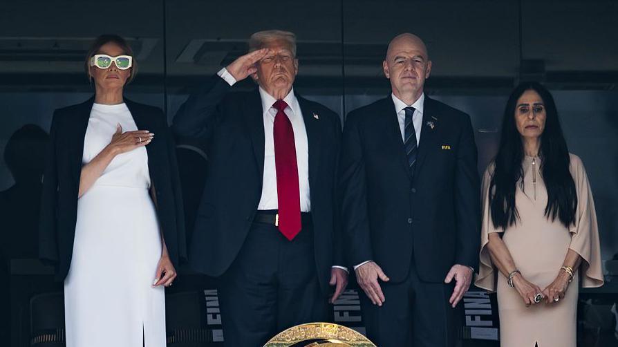 Melania Trump wears a white dress and white glasses standing beside Trump who is saluting and, Gianni Infantino and a woman