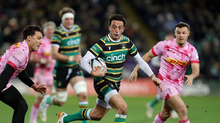 Alex Mitchell carries the ball into space as two Harlequins defenders look on.