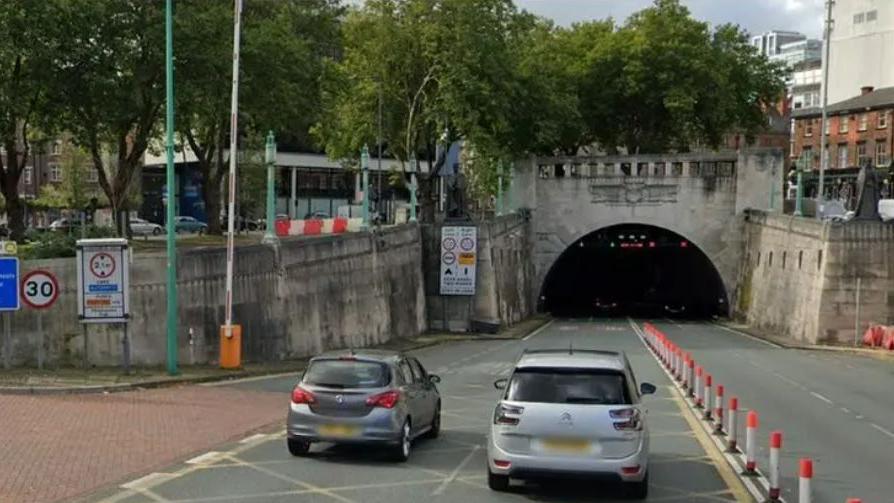 Two cars heading towards a tunnel on a road 