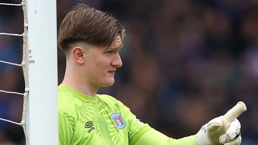 Gabriel Breeze, while in action for Carlisle United, leaning on his goalpost while holding his left hand out, raising his index finger towards a team-mate