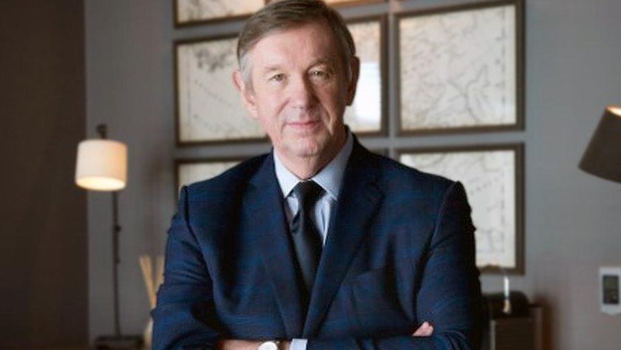 Ken McCulloch standing with crossed arms, wearing a dark blue suit and dark tie