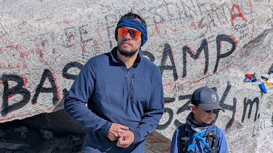 Jake and Rio are standing in front of a large rock at Everest Base Camp.