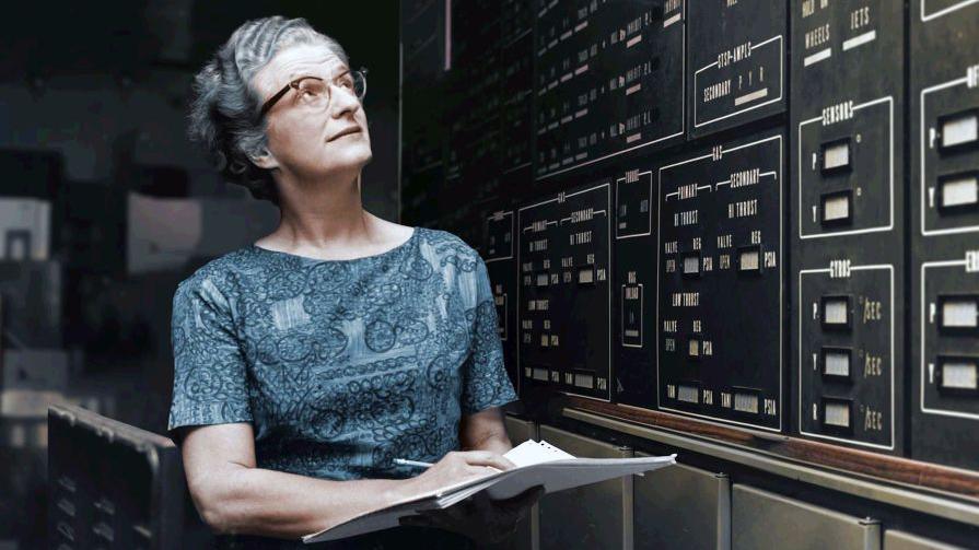Nancy Grace Roman staring at old fashioned technology with a pen and paper in her hands.