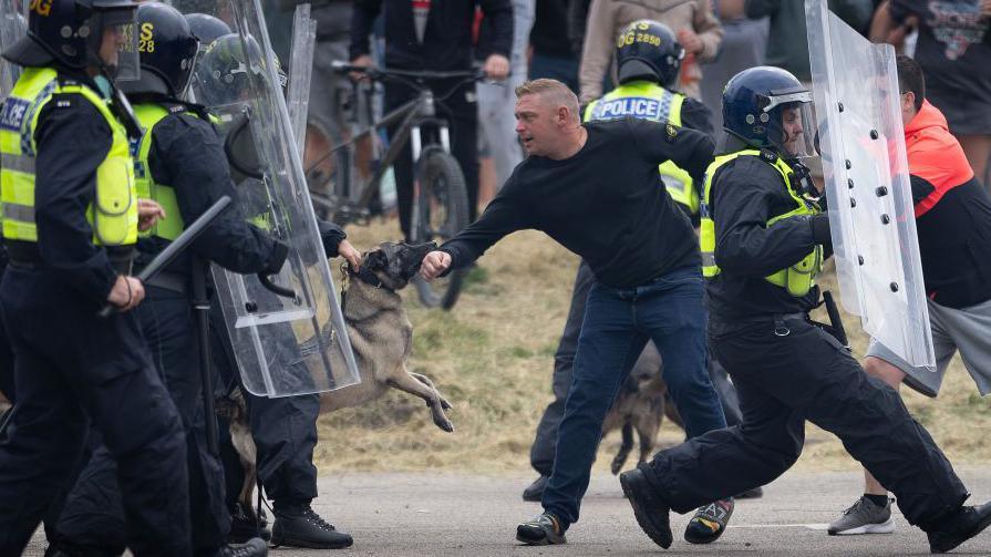 A man being restrained by police, with a police dog biting his arm