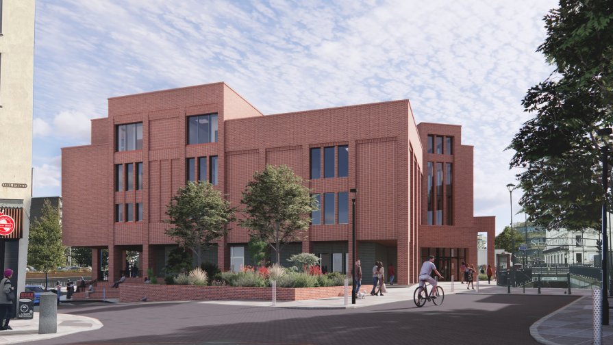 A computer generated image of a red brick building with several windows of different sizes. It sits in the middle of a square with trees and plants in planters and people walking and cycling past it.