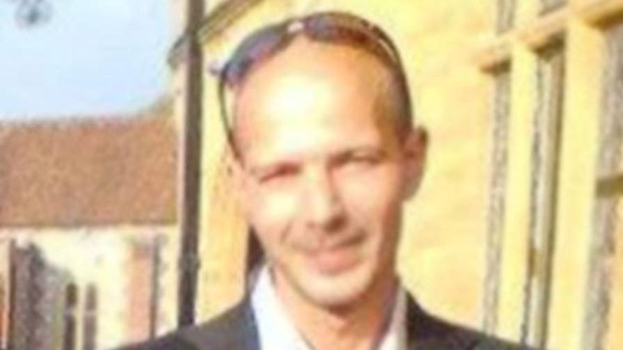 A blurry image of Charlie Rowley. He wears a dark suit and has no hair with sunglasses on his head.