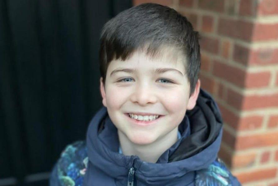 Harry Goulden is seen from the neck up, smiling at the camera. He is wearing a coat with a schoolbag over his shoulders.