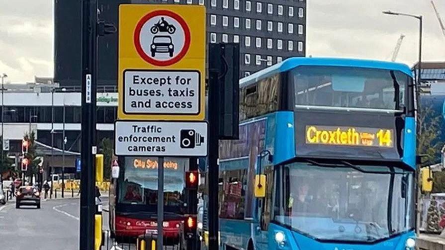 Sign for traffic enforcement cameras in busy road with two double-decker buses 