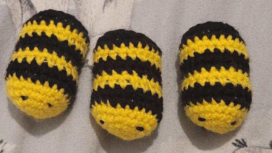 Three close up crocheted little bees. They are oval with yellow bodies and black lines with little black eyes.