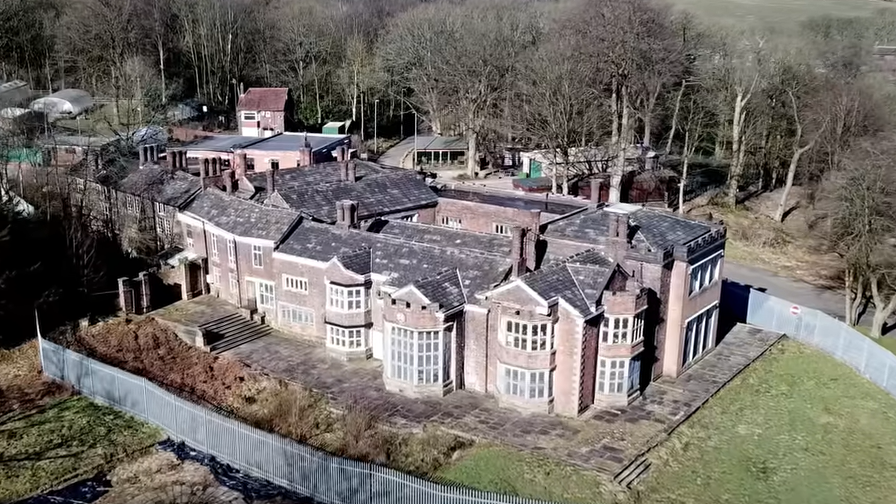 An aerial shot of Hopwood Hall in Middleton, Rochdale. It is a large manor house surrounded by a metal fence and countryside. 