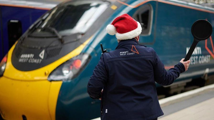 A picture of a train conductor wearing a Santa hat 