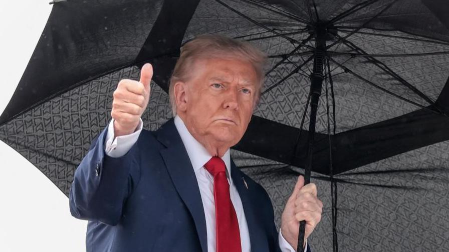 Donald Trump gives a thumbs up as he holds an umbrella before boarding Air Force One