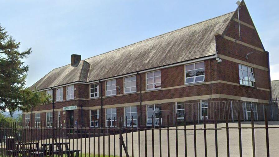 Outside of Ysgol Tryfan - a large two-storey building with yard areas outside, and surrounded by railings 