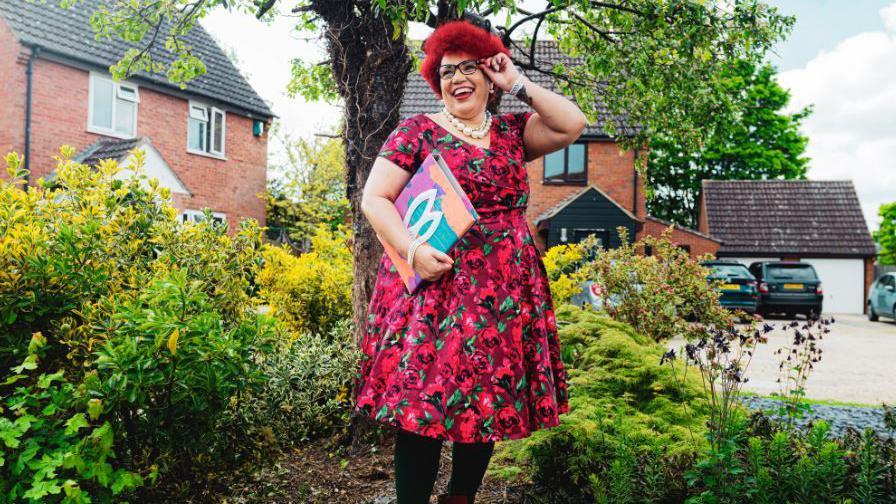 A woman in a red and black dress standing in front of a tree.