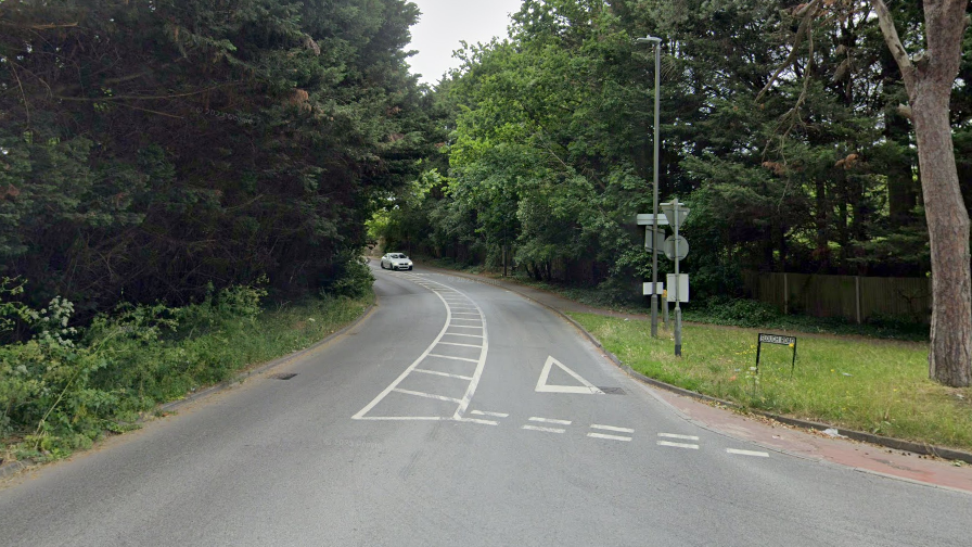 A car approaching a junction on Slough Road, which is surrounded by trees 