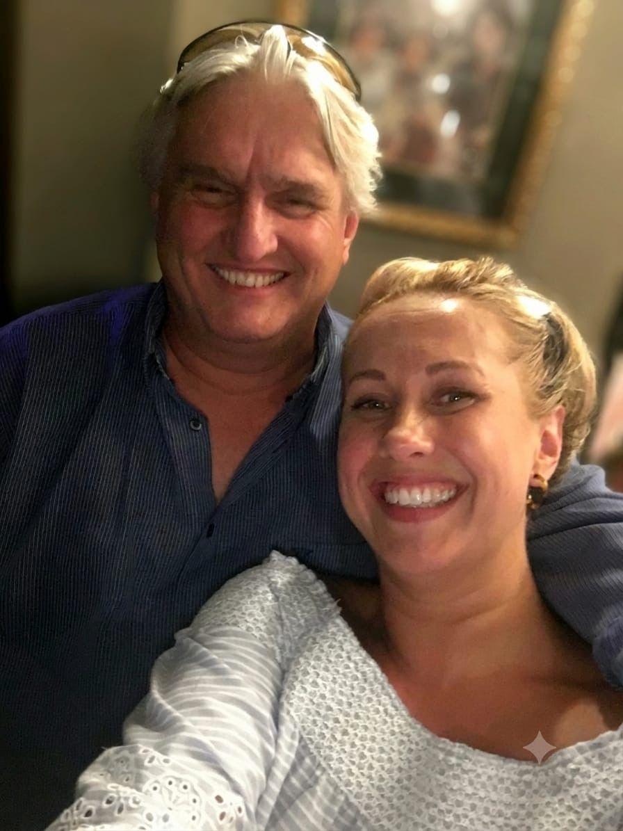 A man with silver hair and sunglasses on his head smiles and the camera with his daughter, who has blonde hair.