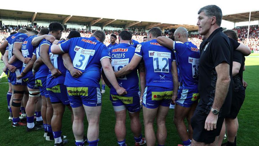 Rob Baxter watches on as Exeter's players take part in a huddle