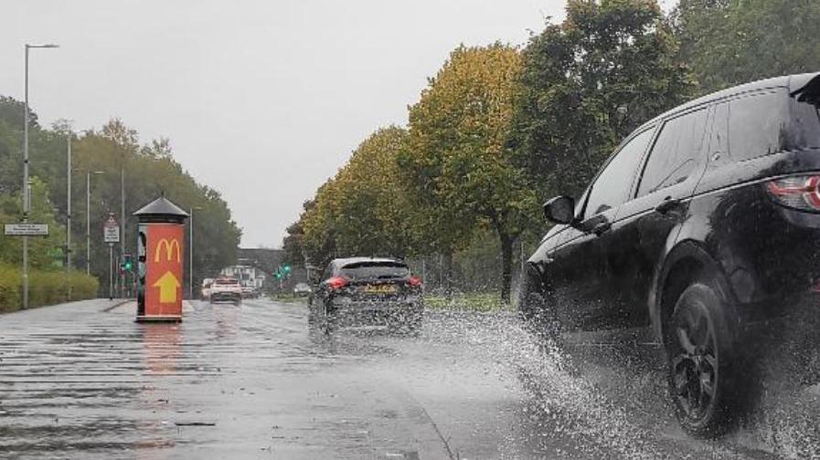 Cars driving on roads with surface water and an advertising board for McDonalds