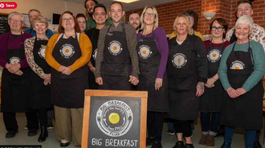 Recipients gathered together wearing black aprons with the Big Breakfast Plus logo on the front, all smiling to camera