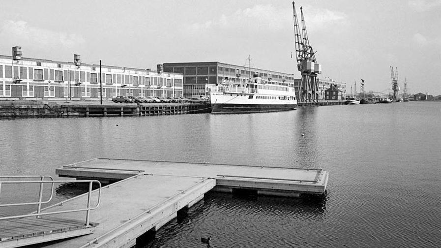 A floating pier on water with warehouses and in the background, cranes for offloading cargo from ships