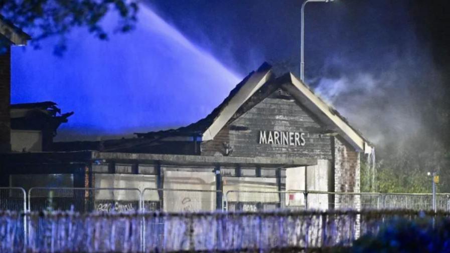 The front of the derelict Mariners Rest pub in Grimsby. Fire damage to the roof is visible as water is sprayed on to it


