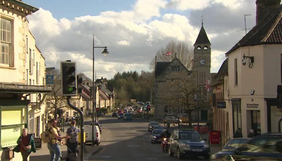 Calne's town cetnre on a sunny day showing a road, traffic lights, historic buildings down the sides and a clock tower