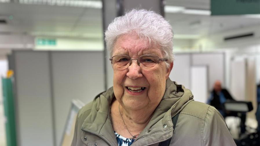 A woman with white hair and glasses looking happy