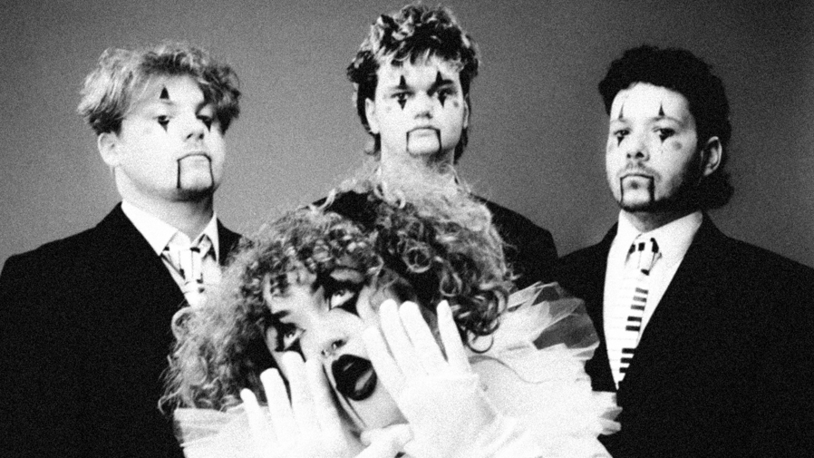 A black and white press image of She's In Parties. The lead singer is at the front of the image while her three fellow band members are standing behind her. They all have a clown face paint on.