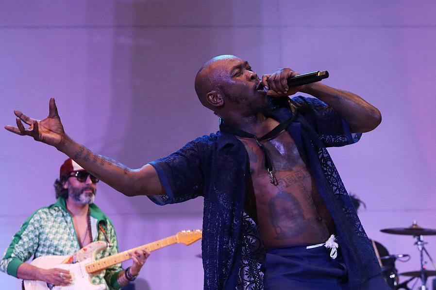 Seun Kuti sings with the microphone, whilst a band member plays the guitar in the background.