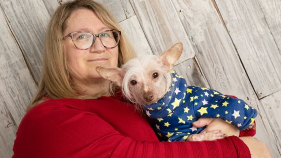 Bev wearing a red sweater holding Muppet- who is wearing a blue dog coat with yellow and white stars on it. 