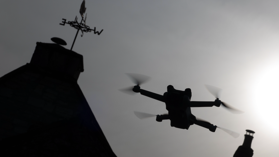 A generic silhouette photograph of a drone in flight near a house.