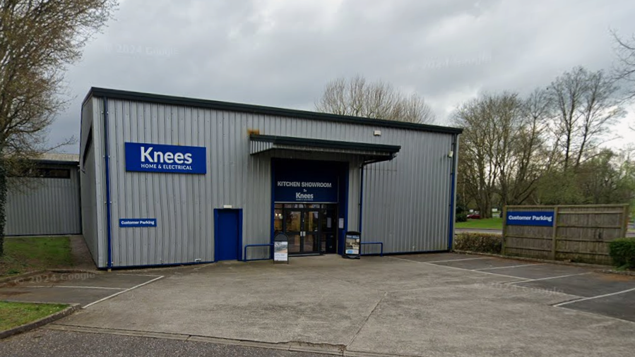 A grey building with a small car park in front. A blue sign says 'Knees home and electrical'