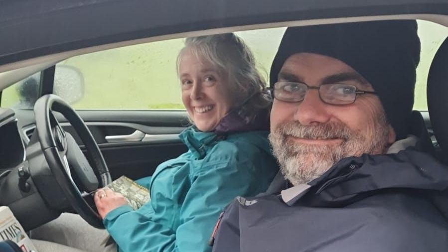 A man and a woman sitting in the front seats of a car smiling at the camera.