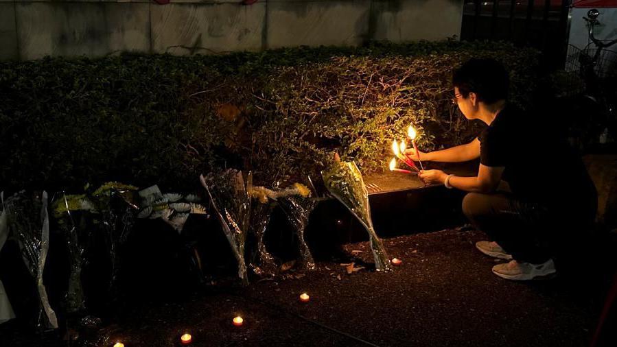 A woman lights candles near floral tributes placed outside a sports centre where a deadly hit-and-run attack took place, in Zhuhai