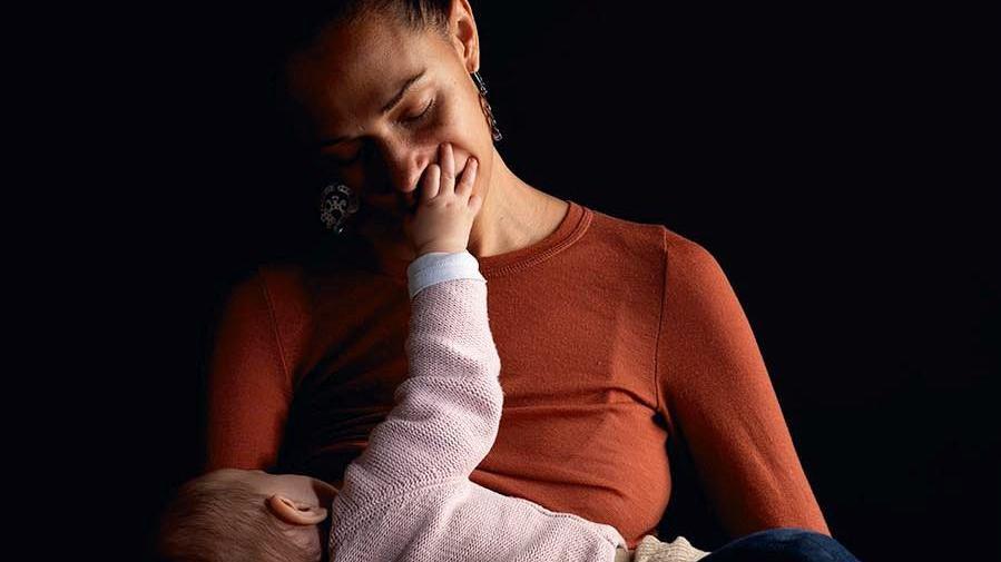 A woman in a red jumper holds a baby as the infant places its hand over her mouth