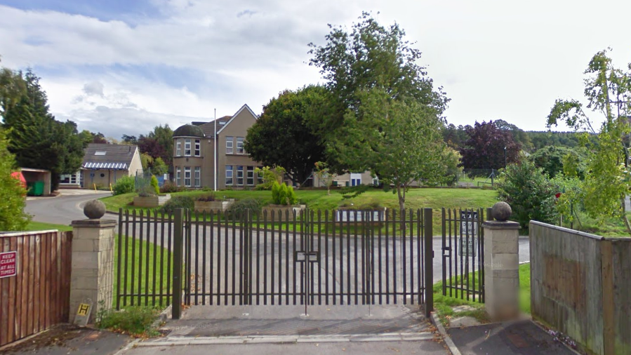 Google images picture of the outside of Fairfield prep school, with iron gates closed in front of the green lawn and school behind. A few green trees block the full view of the front of the school.