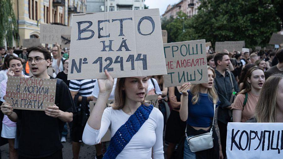 Young Ukrainians in Kyiv hold placards, including a young woman with a white T-shirt and a blue sash