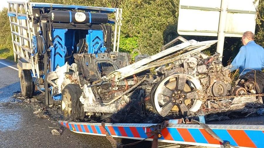 The aftermath of the fire shows a mangled metal on a trailer with burnt tyres and twisted debris.