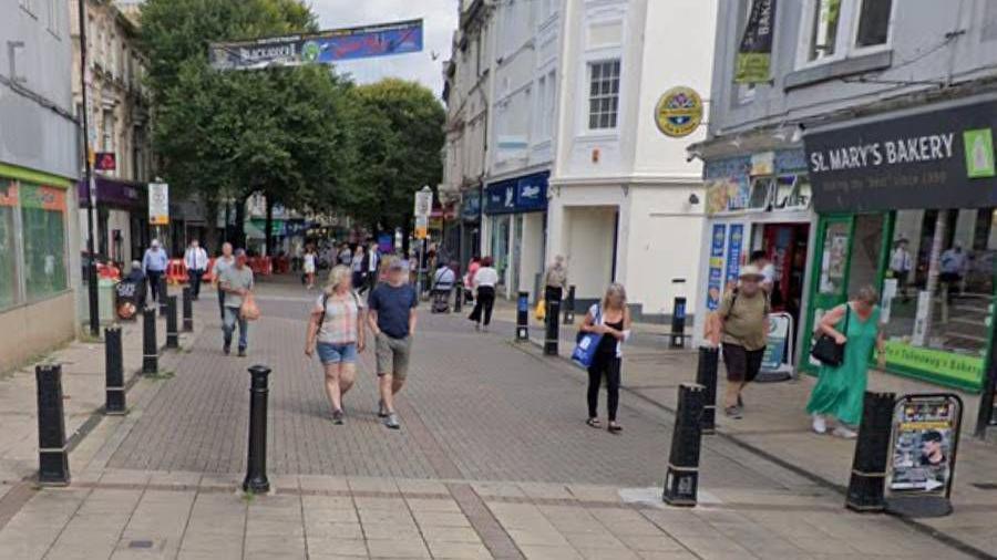 Victoria Street with a number of bollards on concrete paving with a few shops on the left and right-hand side.