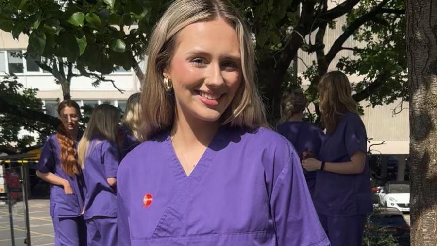 Student nurse Chloe Adams stood in nursing clothing in front of a tree